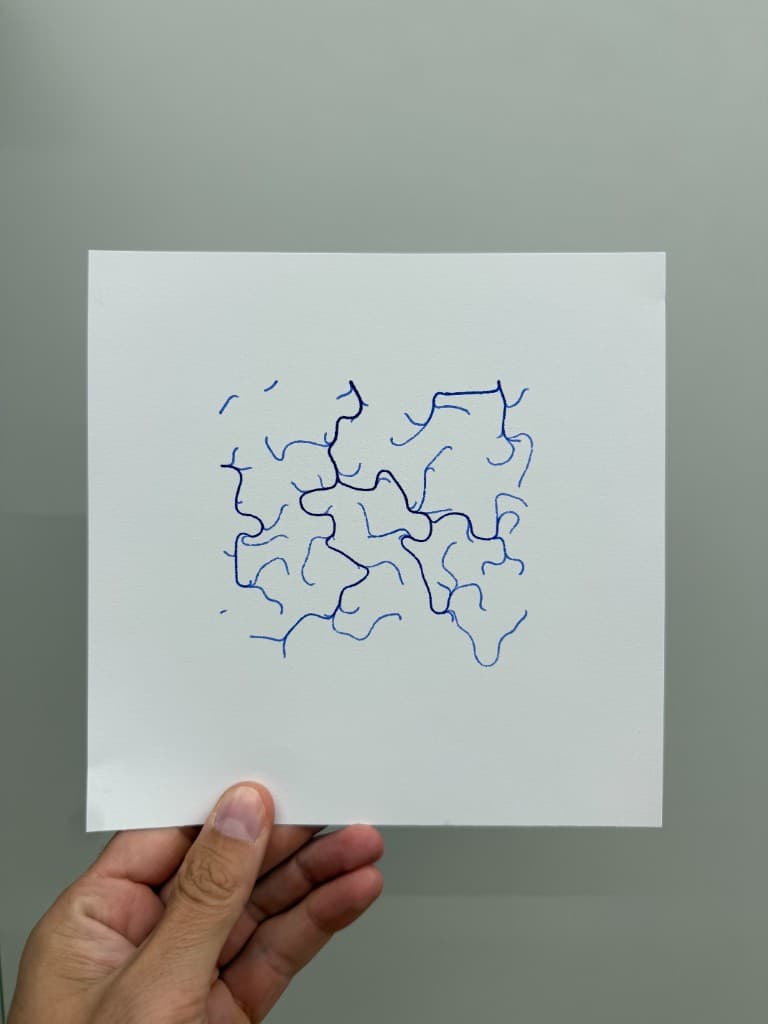 Hand holding pen-plotted branching blue Current linework on white cardstock