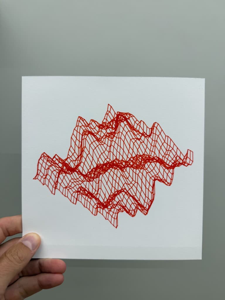 Hand holding pen-plotted red wireframe mountain terrain on white cardstock