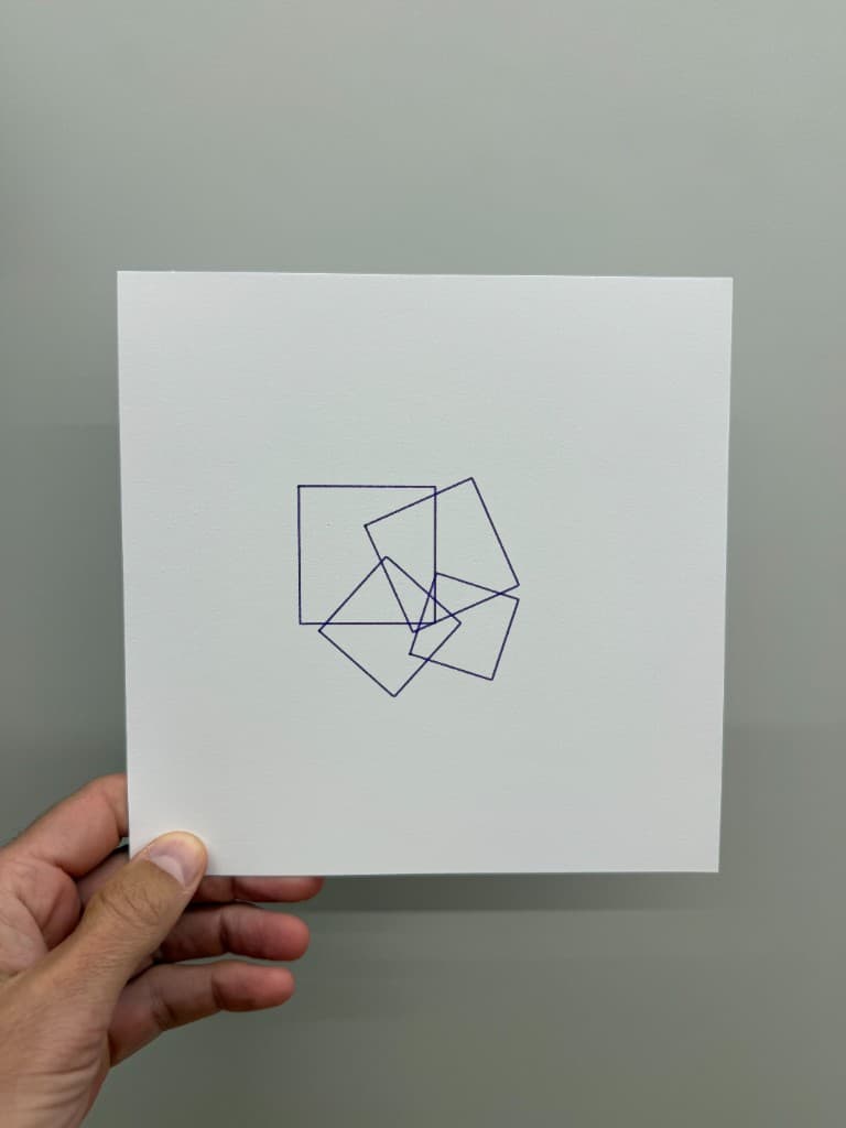 Hand holding pen-plotted purple overlapping rotated squares on white cardstock
