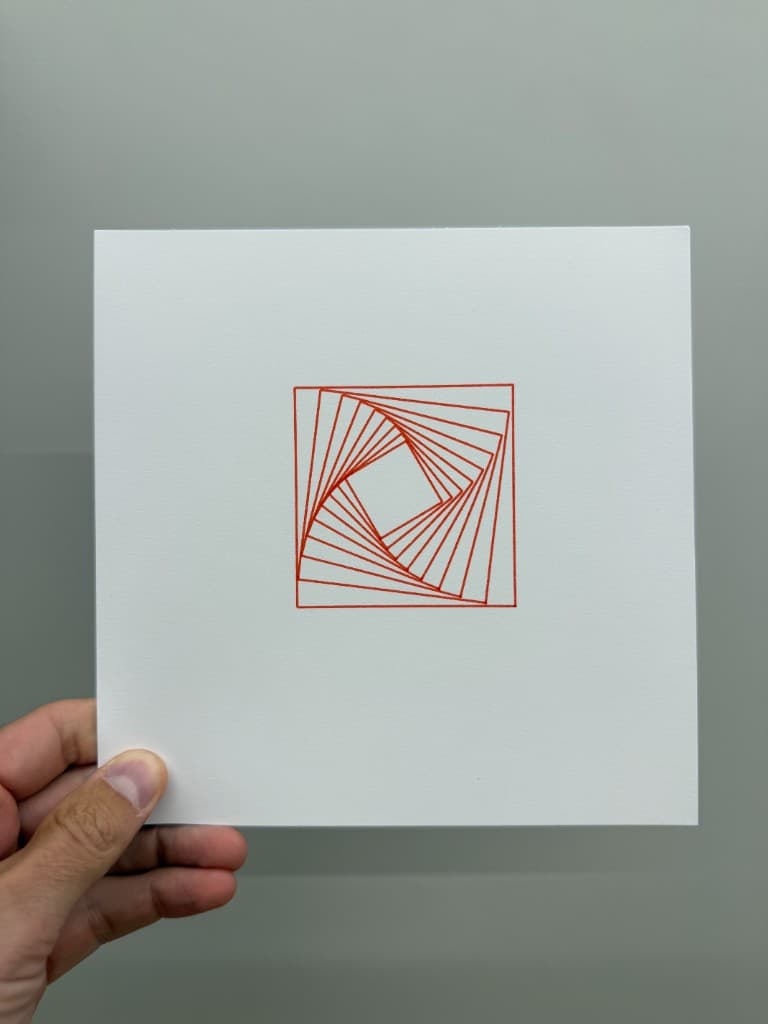 Hand holding pen-plotted red nested square spiral on white cardstock