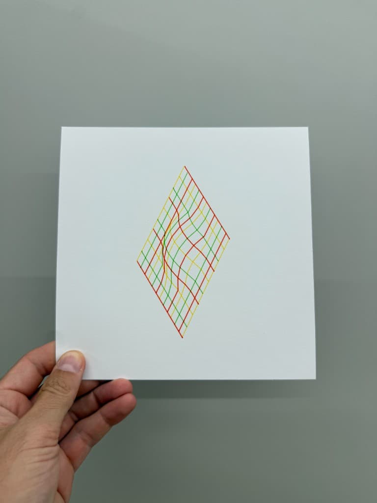 Hand holding pen-plotted diamond surface in red, yellow, and green ink on white cardstock