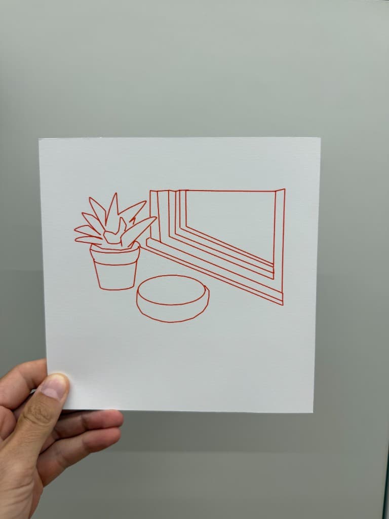 Hand holding pen-plotted red still life with succulent, bowl, and window frame on white cardstock